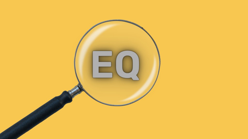 This is an image of a magnifying glass with EQ in the lens and a yellow background. It signifies searching for the signs of emotional intelligence. 