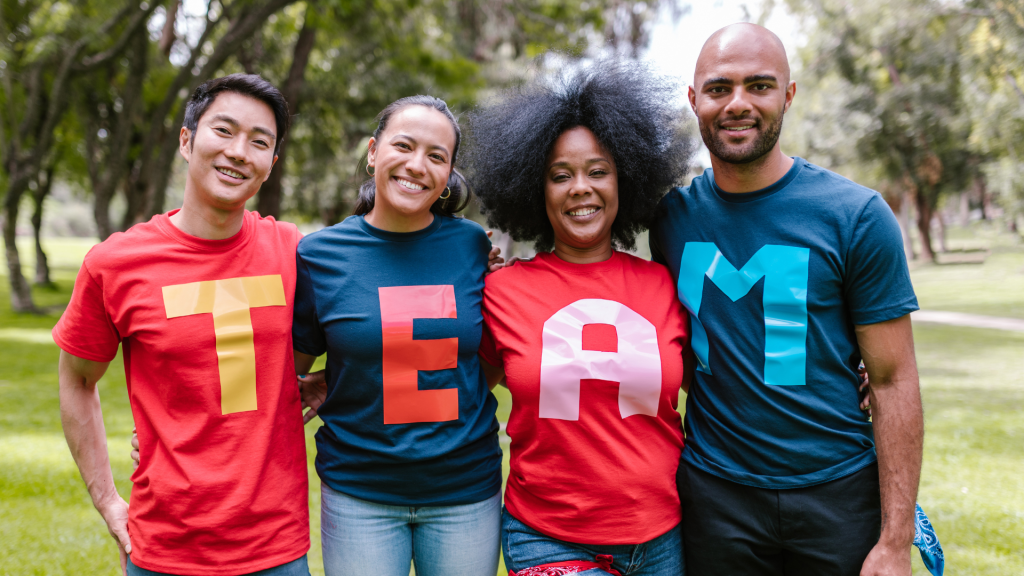 This is a photo of 4 people standing in a line. Each person has a t shirt on with a letter on it spelling out the word TEAM. 